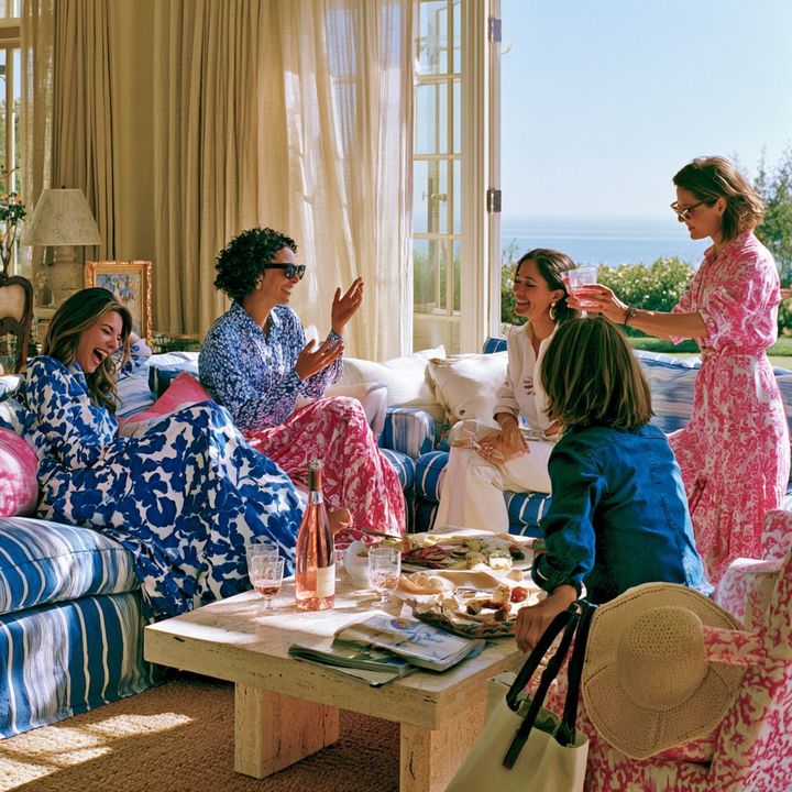 Friends in blue floral dresses chatting in a sunlit sitting room
